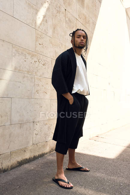 Jeune homme afro-américain à la mode dans une tenue élégante posant sur la rue près d'un mur grincheux — Photo de stock