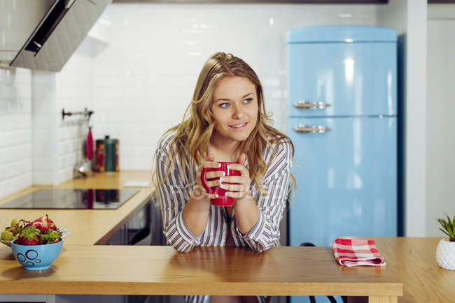Young woman holding hot tea in kitchen — Stock Photo