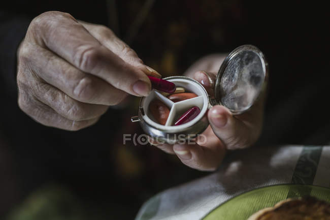 Cropped image of woman taking red pill from steel pill box — Stock Photo