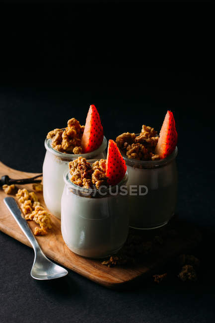 Óculos de leite frio saboroso e deliciosa granola com morangos em tábua de madeira sobre fundo preto — Fotografia de Stock