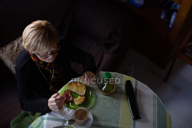 From above aged woman drinking coffee from glass at breakfast while sitting at table — Stock Photo