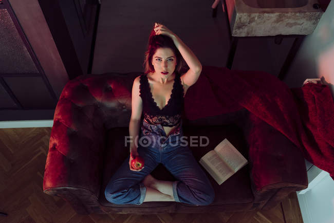 Junge sexy Frau sitzt auf Sofa mit Apfel und Buch — Stockfoto