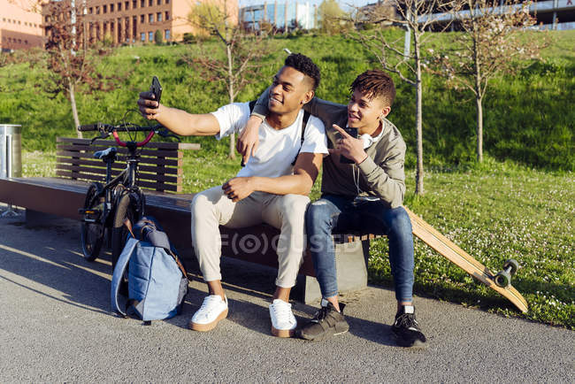 Giovani uomini neri seduti su panchina con smartphone — Foto stock