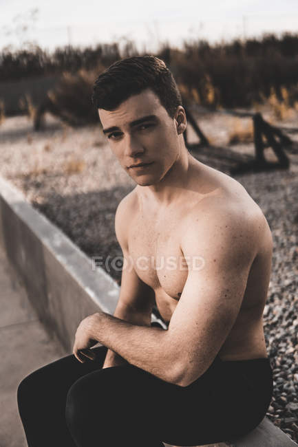 Muskulöser, hemdsloser Typ, der während des Trainings auf der Straße in die Kamera blickt, während er sich an eine Betonmauer lehnt — Stockfoto