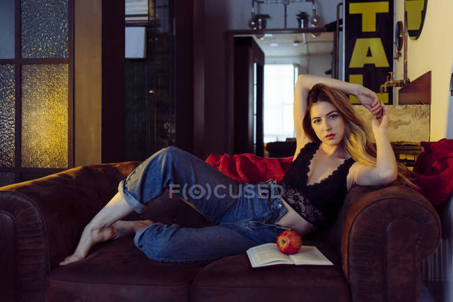 Junge sexy Frau sitzt auf Sofa mit Apfel und Buch — Stockfoto