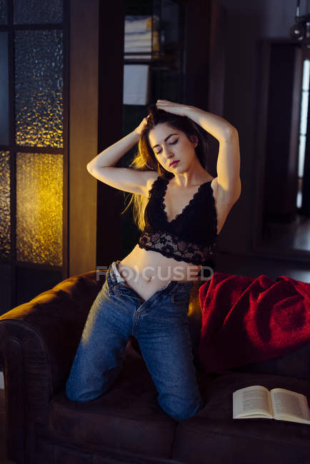 Junge sexy Frau steht auf Knien auf Sofa mit Apfel und Buch — Stockfoto