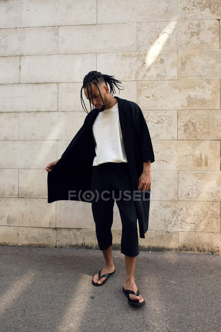 Fashionable young African American male in stylish outfit posing on street near grungy wall — Stock Photo