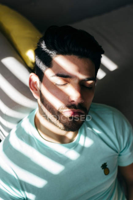 De cima jovem cansado deprimido sozinho macho em camisa casual sentado no sofá em casa e olhando para a câmera — Fotografia de Stock