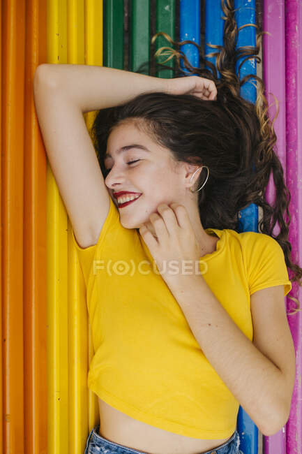 Muito jovem fêmea em roupa casual alegremente fechado olhos enquanto deitado no arco-íris banco de fundo — Fotografia de Stock