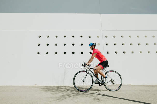Female in helmet and sportswear riding bike on city street on sunny day — Stock Photo