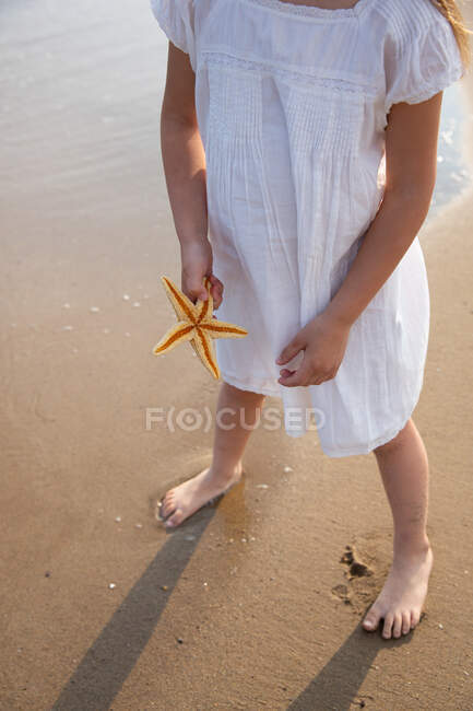 Unerkennbares Mädchen hält Seestern an Sommertag an der Küste — Stockfoto