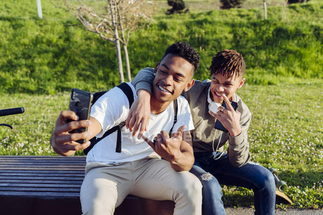 Jeunes hommes noirs assis sur un banc avec smartphone — Photo de stock