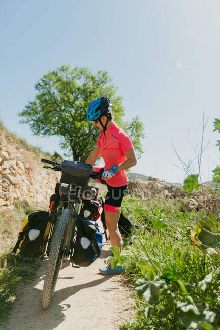 Dame en vêtements de sport et casque équitation vélo sur le chemin pierreux tout en voyageant à travers la forêt par une journée ensoleillée dans la campagne — Photo de stock