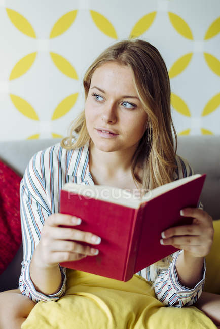 Young happy woman reading book on sofa — Stock Photo