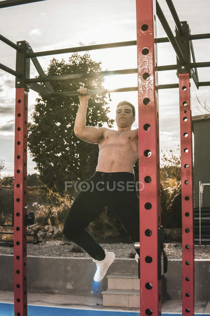 Shirtless young guy performing pull ups on bar during workout on city street on sunny day — Stock Photo