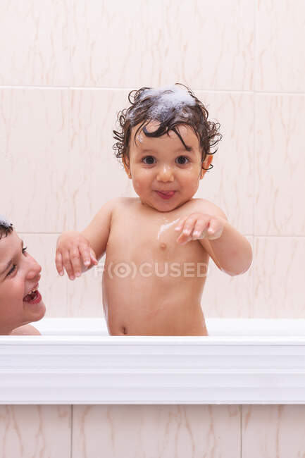 Side view of boy blowing bubble in face of cute baby while taking bath together — Stock Photo