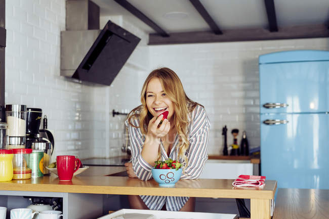 Young woman eating strawberry in kitchen — Stock Photo