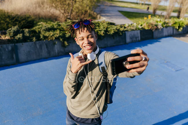 Dall'alto giovane uomo bello allegro nero in abiti casual che mostra il segno della mano shaka e scattare selfie con lo smartphone — Foto stock