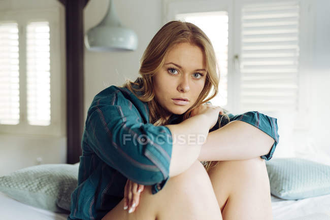 Mujer joven sentada en la cama - foto de stock
