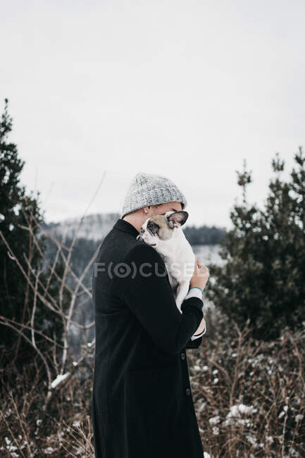 Vue latérale de jeune femelle en manteau chaud décontracté embrassant adulte triste beau chien sur la table sur la plage de pierre LIBÉRATION — Photo de stock