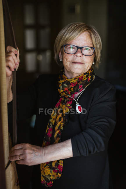 Seniorin mit freundlichem faltigem Gesicht, Brille und Blick in die Kamera, während sie Zeit zu Hause verbringt — Stockfoto