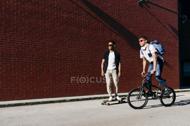 Young African American men riding bicycle and skateboard — Stock Photo