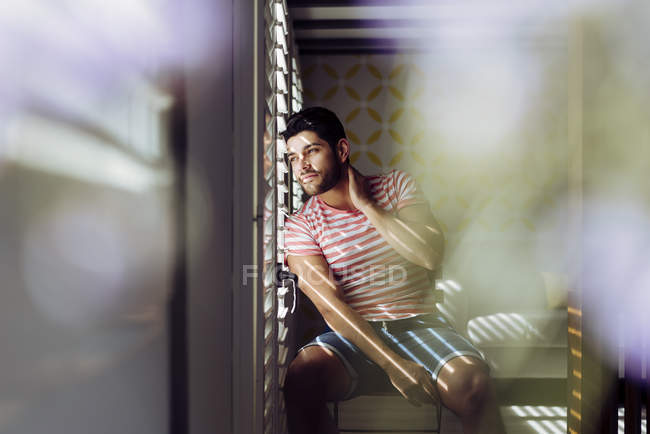 Young alone male in casual clothes sitting on chair and looking out of a window — Stock Photo