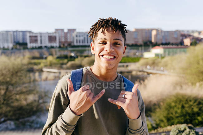 Jovem alegre homem bonito preto com cabelo afro em vestuário casual de pé na rua e mostrando sinal de mão shaka — Fotografia de Stock