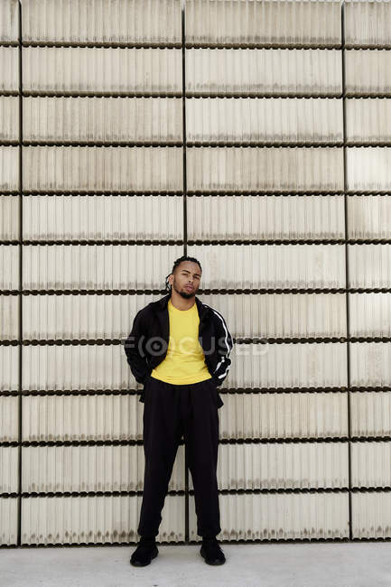 Young African American guy in trendy sportswear looking at camera while standing near cement blocks on city street — Stock Photo