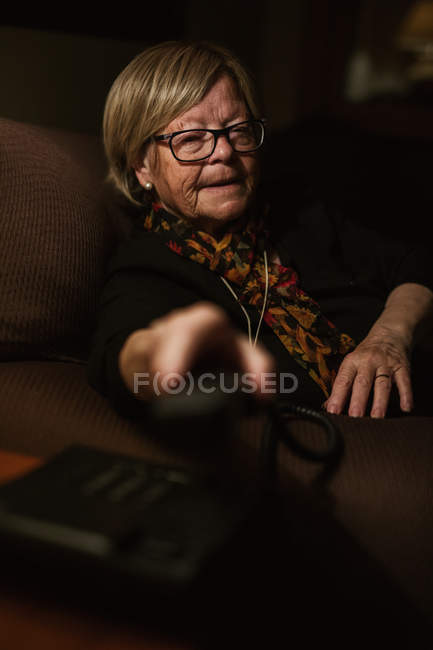 Elderly woman answering phone call while sitting in dark room in evening at home — Stock Photo