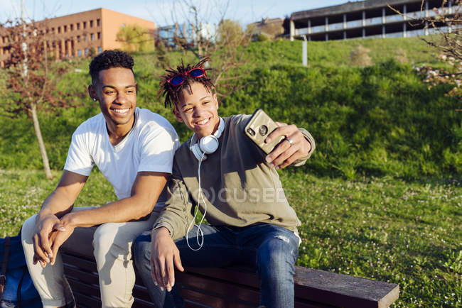 Jovens negros sentados no banco com smartphone — Fotografia de Stock