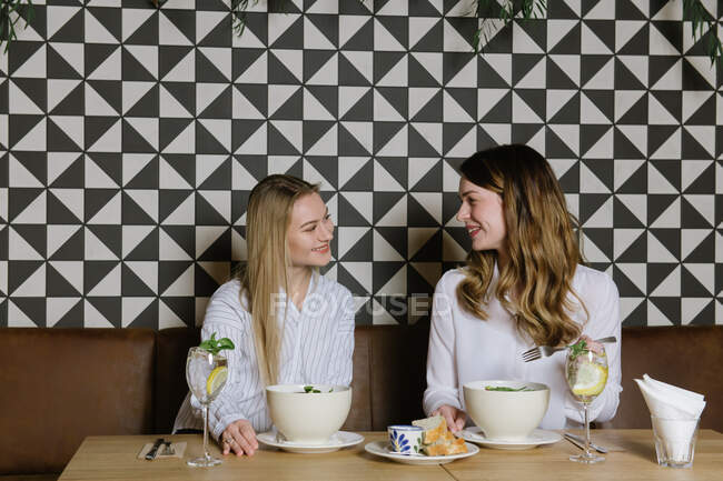Deux jolies dames souriantes et ayant un déjeuner sain dans un restaurant confortable ensemble — Photo de stock