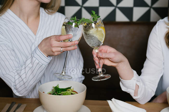 Vista Crop di donne anonime bicchieri di cocktail alcolici mentre pranzano insieme in un accogliente ristorante — Foto stock