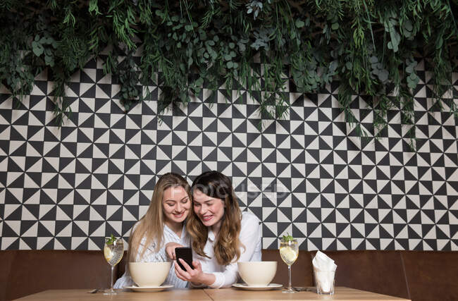 Элегантные подруги по телефону сидят за столом ресторана во время обеда — стоковое фото