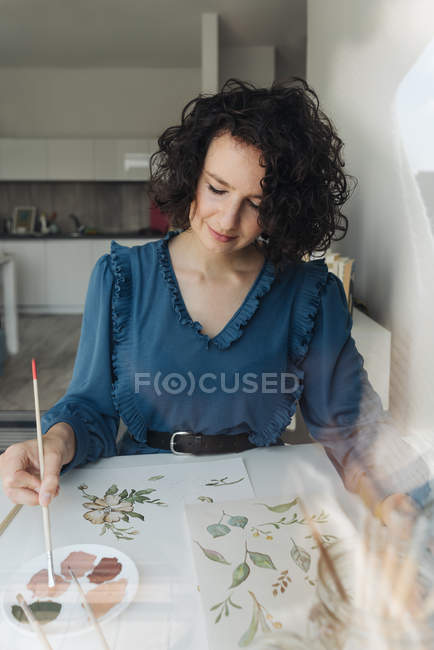 Elegante donna con pennello pittura ad acquerello fiori su foglio alla scrivania — Foto stock