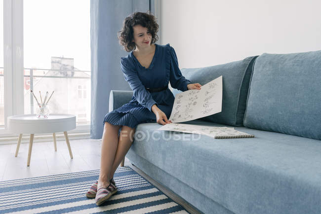 Bella giovane bruna seduta sul divano e alla ricerca di album con disegni a casa — Foto stock