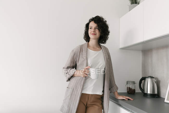 Elegante mujer pensativa en la sala de estar moderna con una taza de café - foto de stock