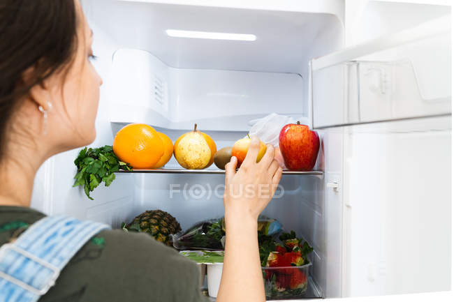 Donna irriconoscibile che prende mela fresca dallo scaffale del frigorifero a casa — Foto stock
