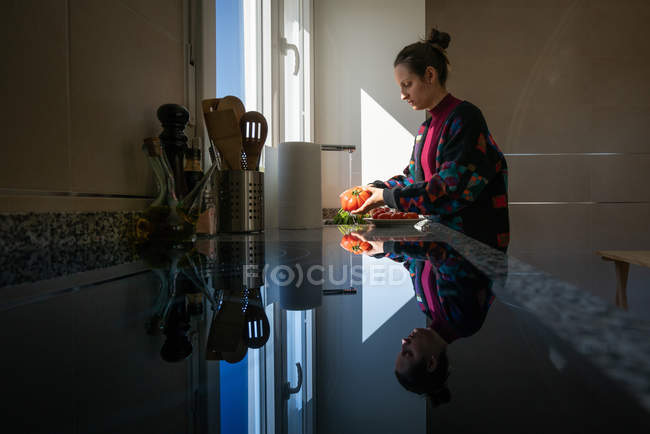 Female in colorful jacket washing fresh tomato under clean water over sink in kitchen at home — Stock Photo