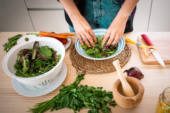 Manos de la mujer preparando verduras mientras cocina ensalada saludable en la cocina - foto de stock