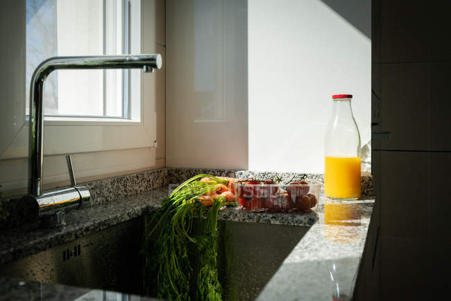 Gemüse und eine Flasche Orangensaft in der Nähe einer Spüle zu Hause — Stockfoto