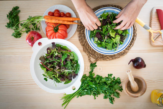 Mains de femme préparant des légumes tout en cuisinant une salade saine dans la cuisine — Photo de stock