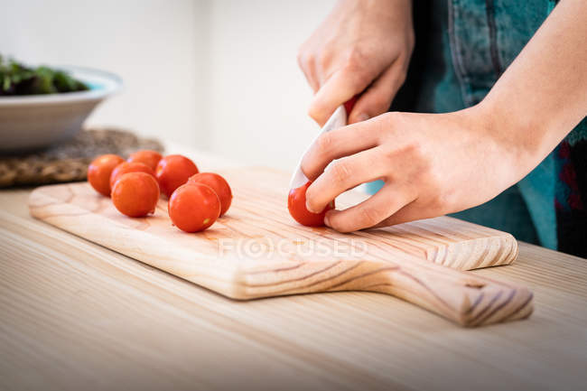 Cropped image of woman cutting tomatoes while cooking healthy salad in kitchen — Stock Photo