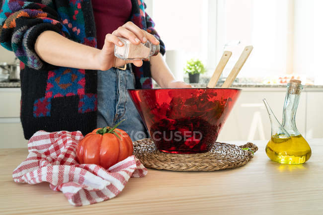 Imagem cortada de mulher em jaqueta multicolorida colocando sal em salada saudável em tigela — Fotografia de Stock