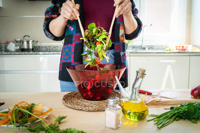 Immagine ritagliata di donna in giacca multicolore mescolando verdure in ciotola durante la cottura di insalata sana in cucina — Foto stock