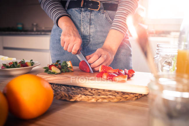 Abgeschnittenes Bild einer Frau in lässigem Outfit, die in einer Küche frische Erdbeeren hackt — Stockfoto