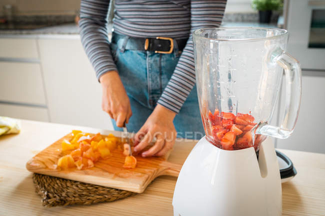 Cropped image of woman in casual outfit chopping fruits for healthy orange and strawberry drink in kitchen at home — Stock Photo