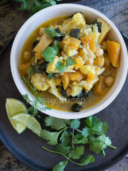 Assiette avec délicieux curry végétarien et tranches de citron vert placées sur un plateau sur fond en bois — Photo de stock