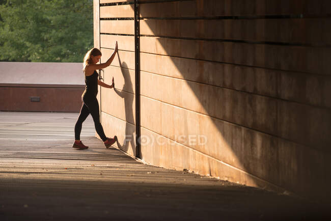 Mujer joven estirándose después de correr y apoyarse en una pared de la calle - foto de stock