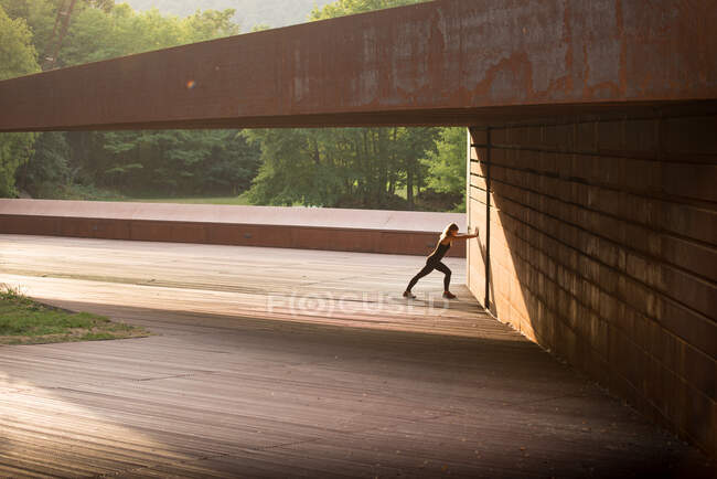 Молода жінка розтягується після бігу і схиляється в дивовижній геометричній будівлі — стокове фото